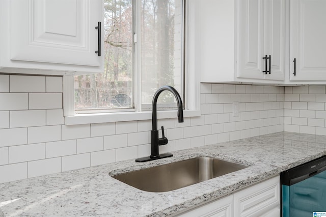 kitchen featuring tasteful backsplash, light stone counters, dishwashing machine, sink, and white cabinetry