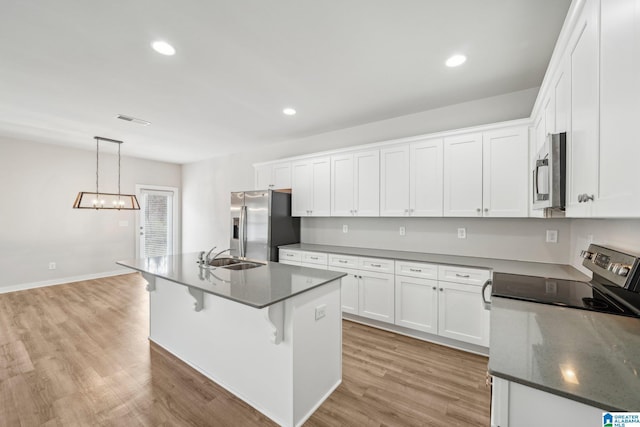 kitchen with appliances with stainless steel finishes, a kitchen island with sink, decorative light fixtures, white cabinets, and light hardwood / wood-style floors