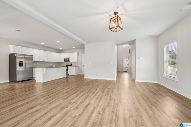 unfurnished living room with beam ceiling, a chandelier, and light wood-type flooring