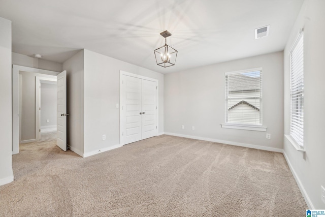 unfurnished bedroom featuring a chandelier, light colored carpet, and a closet