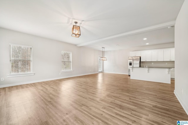 unfurnished living room featuring beam ceiling and light hardwood / wood-style flooring