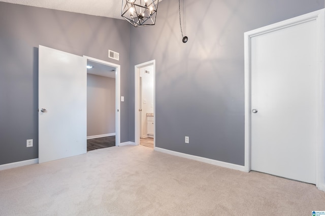 unfurnished bedroom featuring a textured ceiling, a towering ceiling, light carpet, and a chandelier