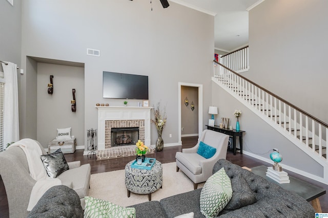 living room with hardwood / wood-style floors, a high ceiling, crown molding, ceiling fan, and a fireplace