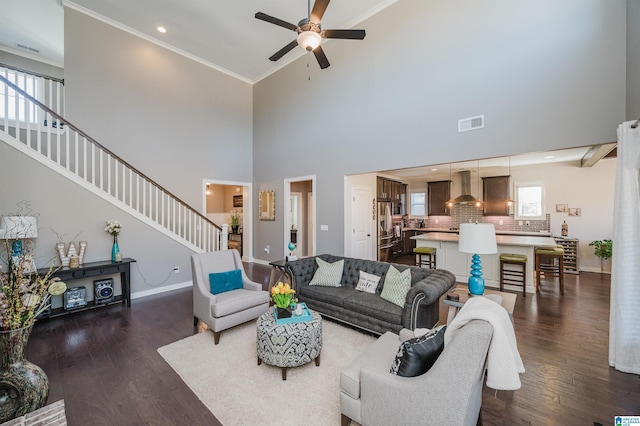 living room featuring dark hardwood / wood-style floors, ceiling fan, a towering ceiling, and crown molding