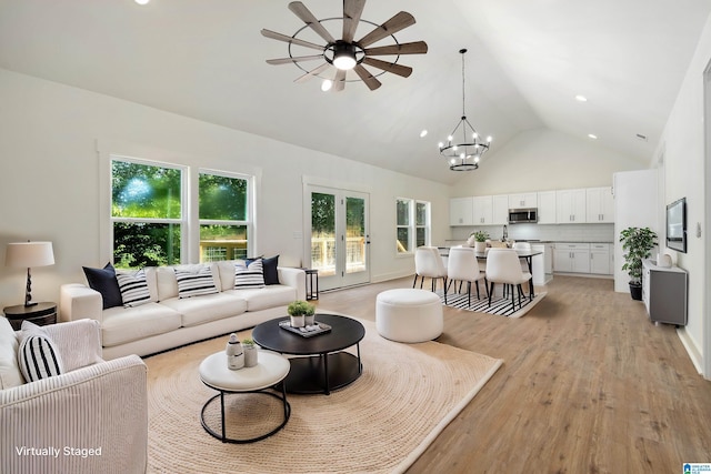 living room with high vaulted ceiling, ceiling fan with notable chandelier, and light hardwood / wood-style floors