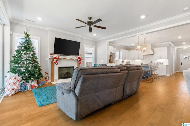 living room with light hardwood / wood-style flooring, a healthy amount of sunlight, ceiling fan with notable chandelier, and ornamental molding