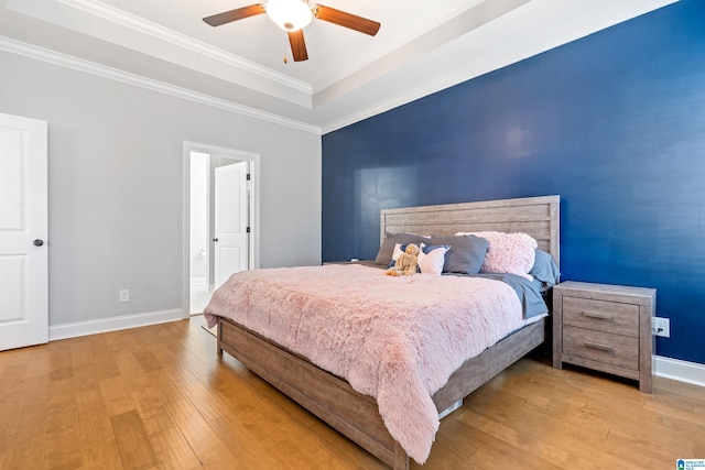 bedroom featuring a raised ceiling, crown molding, light hardwood / wood-style flooring, and ceiling fan