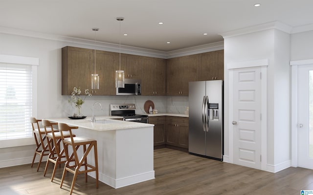 kitchen featuring hardwood / wood-style floors, decorative light fixtures, a breakfast bar area, appliances with stainless steel finishes, and ornamental molding