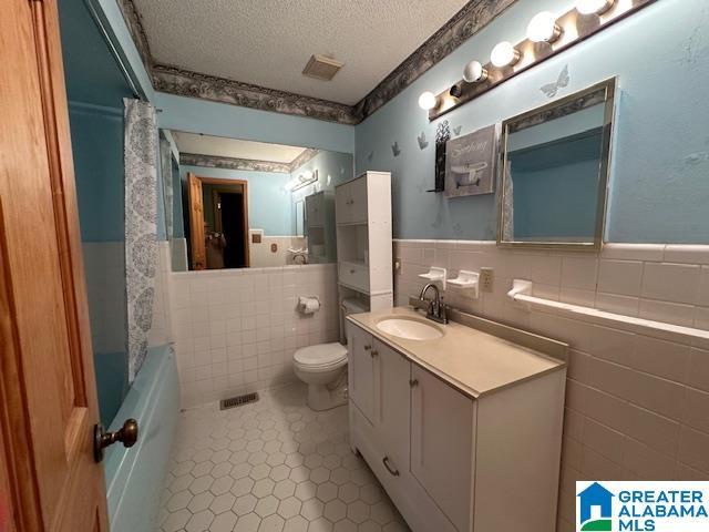 full bathroom with vanity, a textured ceiling, tile walls, tile patterned flooring, and toilet