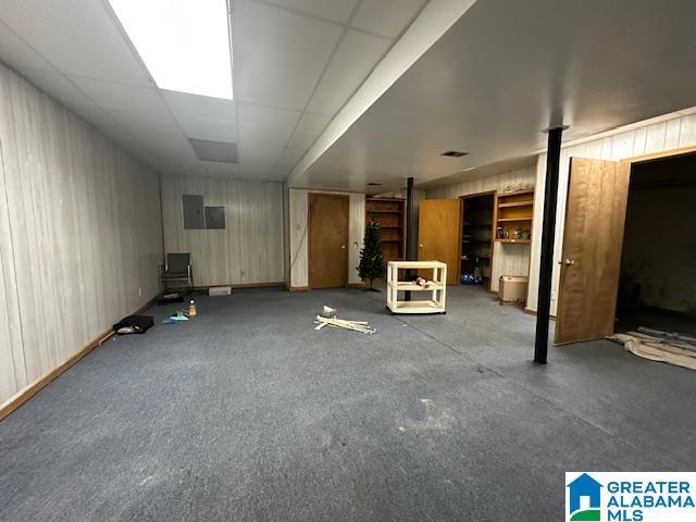 basement with wooden walls, a drop ceiling, and electric panel