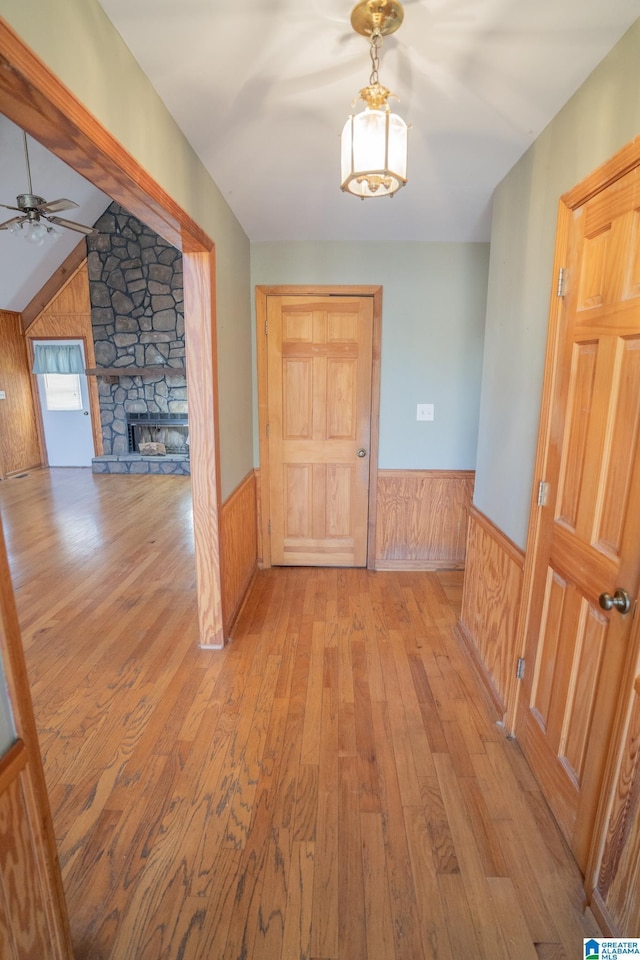 corridor featuring wood walls, light hardwood / wood-style floors, and vaulted ceiling