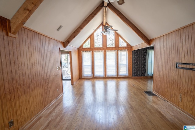 unfurnished living room with vaulted ceiling with beams, ceiling fan, wood walls, and light hardwood / wood-style flooring