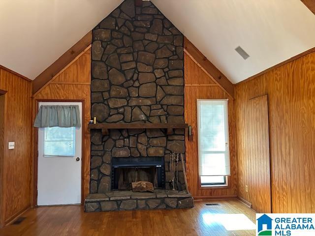 unfurnished living room with a stone fireplace, wood walls, high vaulted ceiling, and hardwood / wood-style flooring