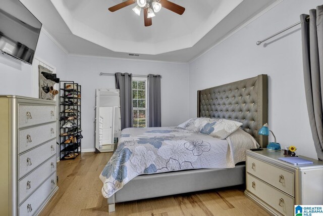 bedroom featuring light hardwood / wood-style floors, a raised ceiling, ceiling fan, and crown molding