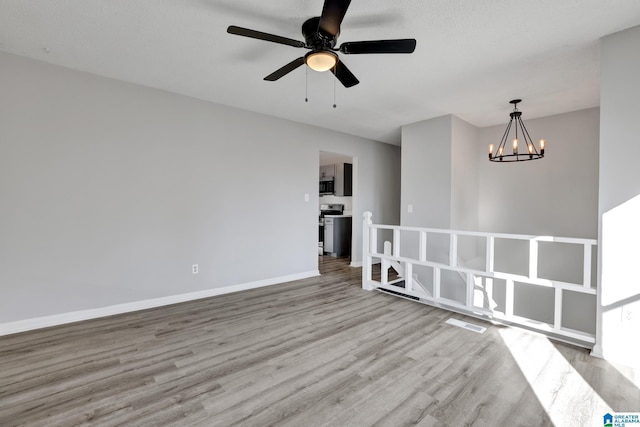 unfurnished room featuring ceiling fan with notable chandelier and light wood-type flooring