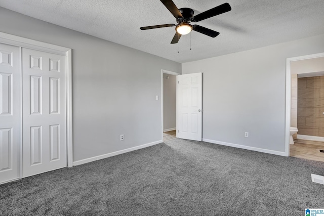 unfurnished bedroom with ceiling fan, ensuite bathroom, a textured ceiling, and dark colored carpet