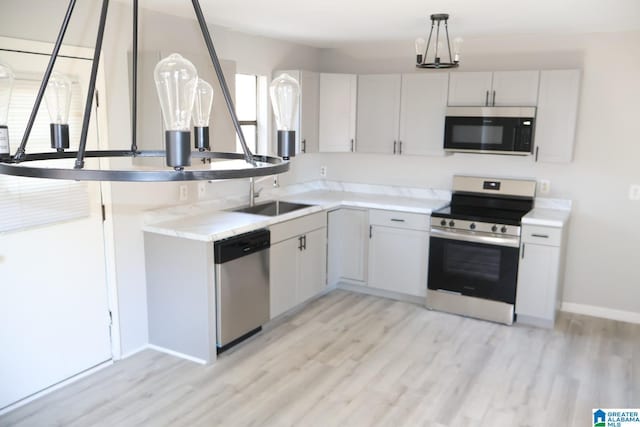 kitchen featuring stainless steel appliances, sink, decorative light fixtures, white cabinets, and light hardwood / wood-style floors