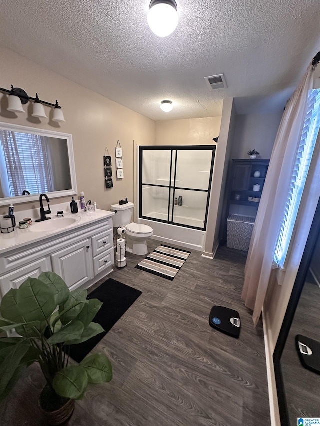 full bathroom featuring a wealth of natural light, bath / shower combo with glass door, a textured ceiling, and hardwood / wood-style flooring