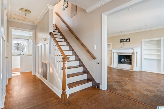 staircase featuring wood-type flooring, crown molding, and sink