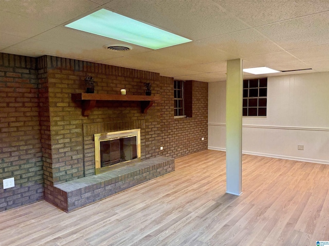 unfurnished living room featuring a fireplace, a paneled ceiling, light hardwood / wood-style flooring, and brick wall