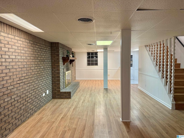 basement with a fireplace, a drop ceiling, wood-type flooring, and brick wall