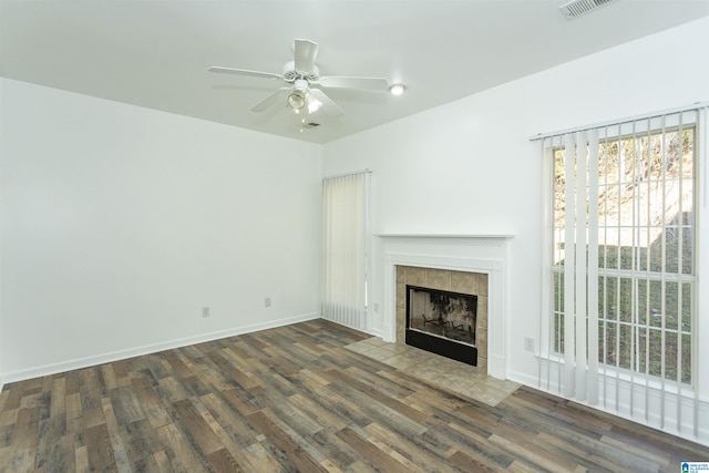 unfurnished living room featuring ceiling fan, dark wood-type flooring, and a tiled fireplace