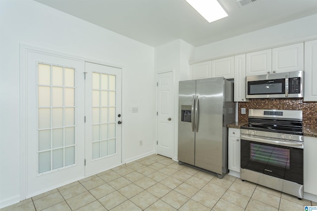 kitchen with decorative backsplash, dark stone countertops, light tile patterned floors, white cabinetry, and stainless steel appliances