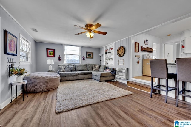 living room featuring ceiling fan, built in features, heating unit, crown molding, and hardwood / wood-style flooring