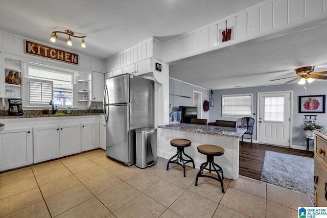 kitchen with a breakfast bar area, stainless steel fridge, white cabinetry, and plenty of natural light