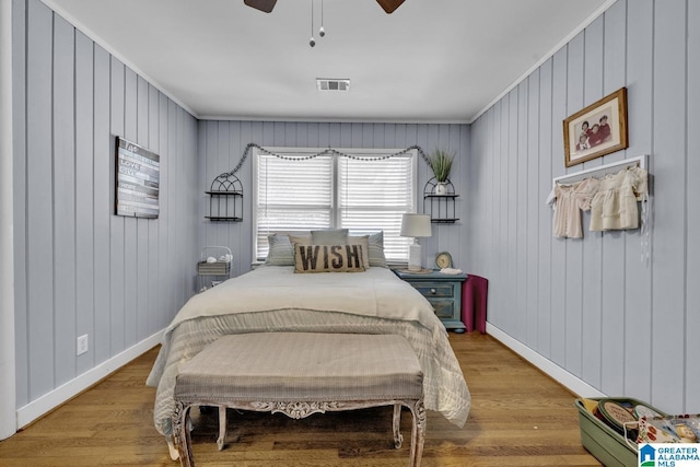 bedroom with ceiling fan, light hardwood / wood-style floors, wood walls, and ornamental molding