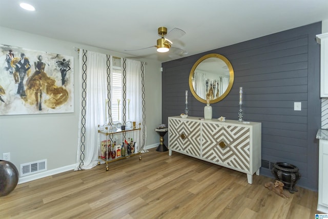 interior space with ceiling fan, wooden walls, and light wood-type flooring