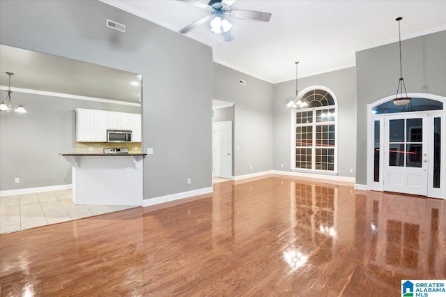 unfurnished living room featuring light tile patterned floors, ceiling fan with notable chandelier, and ornamental molding