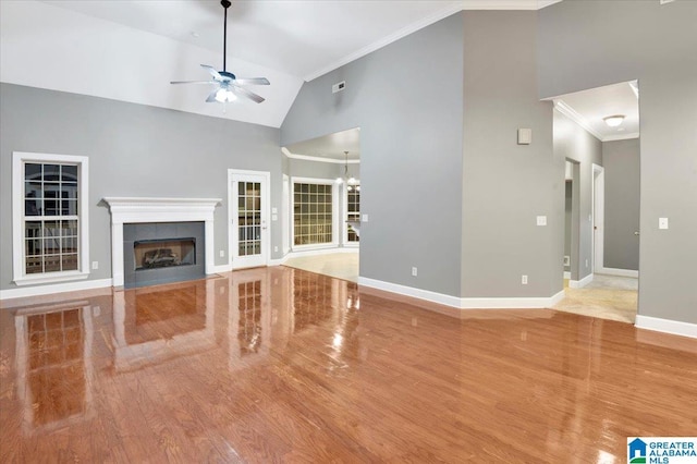 unfurnished living room with a tile fireplace, ceiling fan with notable chandelier, high vaulted ceiling, and ornamental molding