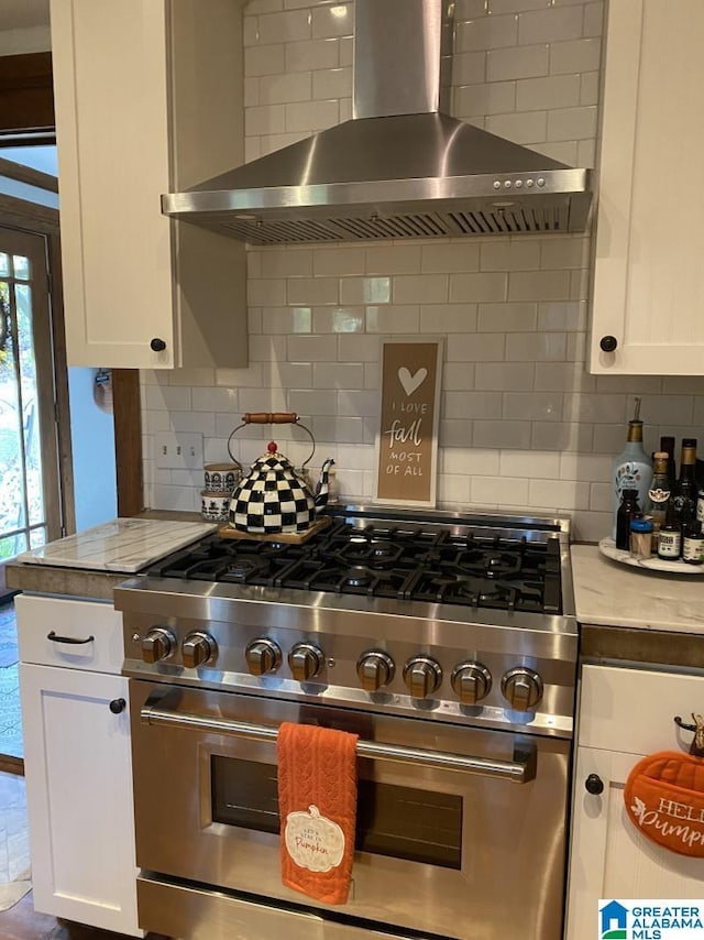 kitchen featuring decorative backsplash, high end range, wall chimney range hood, and white cabinetry