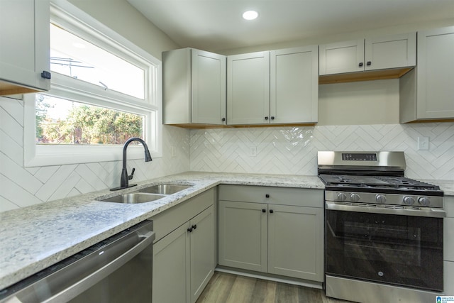 kitchen with backsplash, sink, light hardwood / wood-style floors, light stone counters, and stainless steel appliances