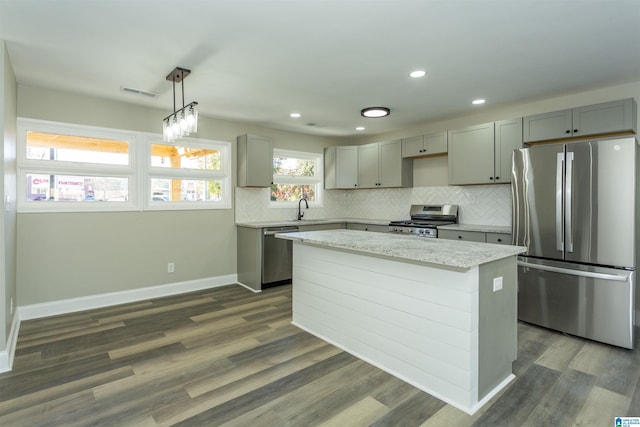 kitchen featuring stainless steel appliances, dark wood-type flooring, sink, decorative light fixtures, and a kitchen island