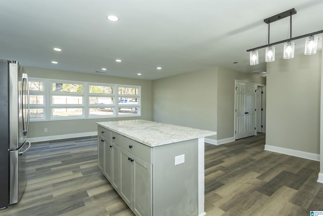 kitchen with light stone counters, a kitchen island, decorative light fixtures, dark hardwood / wood-style floors, and stainless steel refrigerator