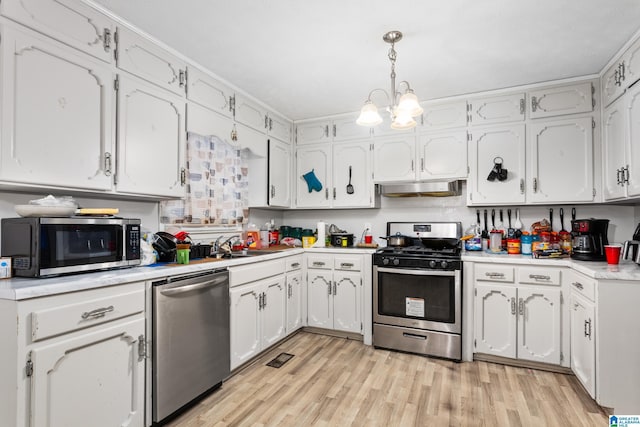 kitchen with light wood-type flooring, stainless steel appliances, an inviting chandelier, white cabinetry, and hanging light fixtures