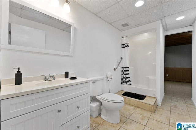 bathroom with a paneled ceiling, tile patterned floors, walk in shower, vanity, and toilet