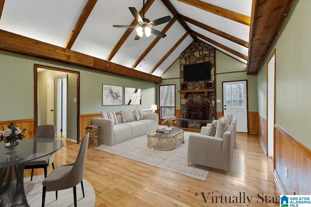 living room with high vaulted ceiling, a stone fireplace, light hardwood / wood-style flooring, ceiling fan, and beam ceiling