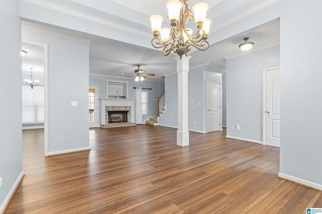 unfurnished living room featuring ceiling fan with notable chandelier, a stone fireplace, crown molding, and dark hardwood / wood-style floors