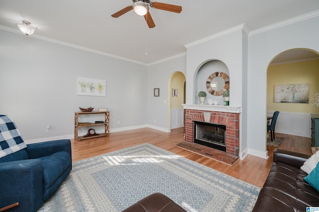 living room featuring hardwood / wood-style floors, ceiling fan, crown molding, and a brick fireplace