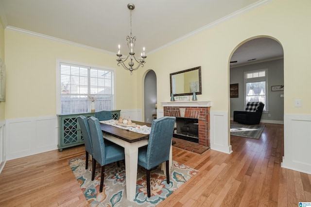 dining room featuring a chandelier, light hardwood / wood-style floors, a brick fireplace, and ornamental molding