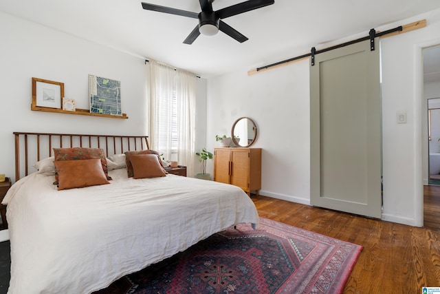 bedroom featuring a barn door, dark hardwood / wood-style floors, and ceiling fan