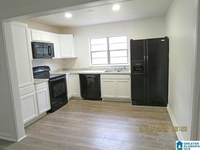 kitchen with wood finished floors, a sink, black appliances, light countertops, and white cabinetry