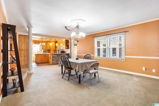 carpeted dining room with ornate columns, ornamental molding, and an inviting chandelier