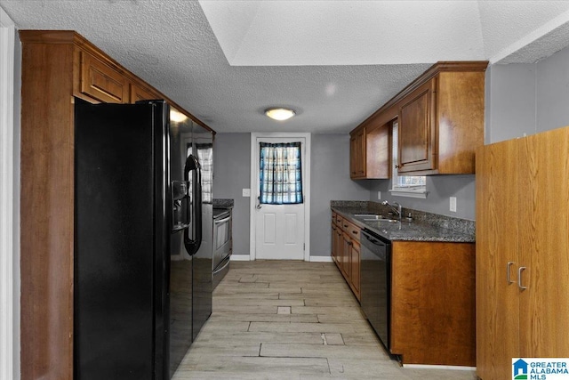 kitchen featuring black appliances, a sink, light wood-style floors, brown cabinetry, and baseboards