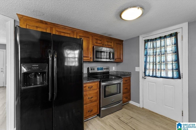 kitchen with dark stone counters, a textured ceiling, appliances with stainless steel finishes, and light hardwood / wood-style flooring