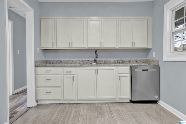 kitchen with white cabinets, dishwasher, light stone counters, and sink