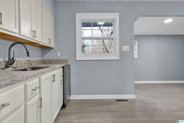 kitchen featuring white cabinets, stainless steel dishwasher, light stone counters, and sink